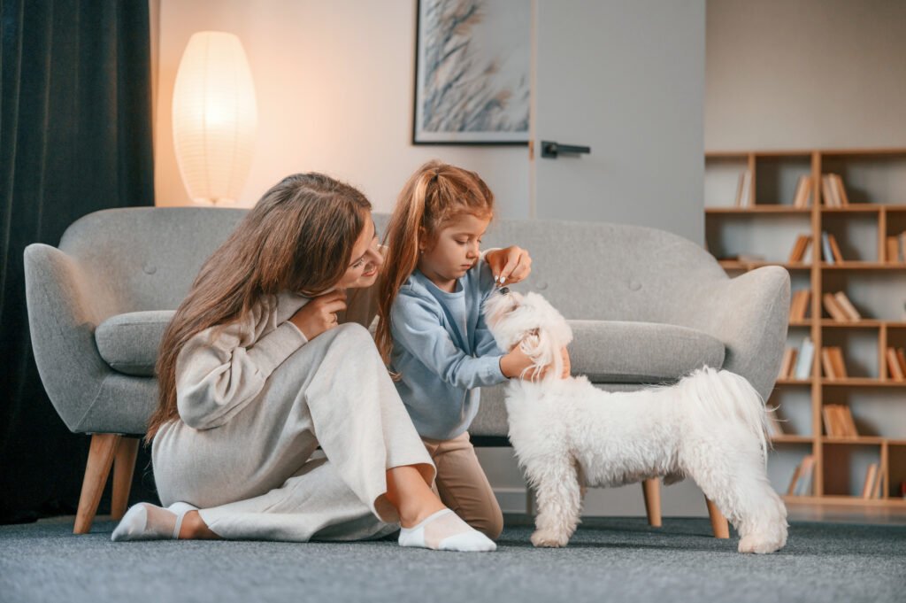 Having fun together. Mother with daughter is at home with maltese dog.